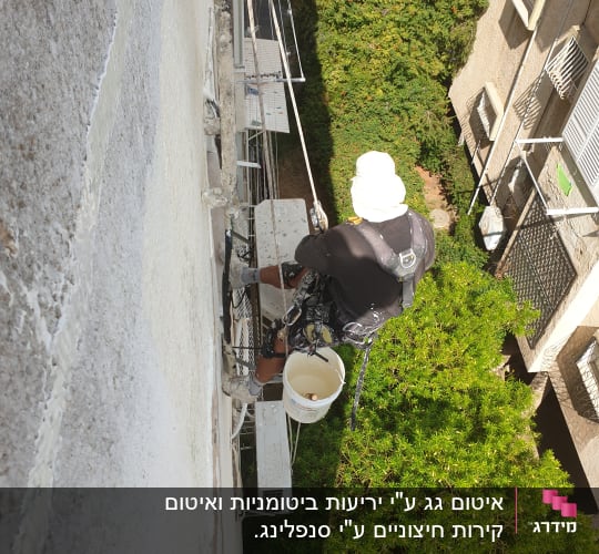 אדם על פיגום עם דלי צבע אוטם קיר חיצוני